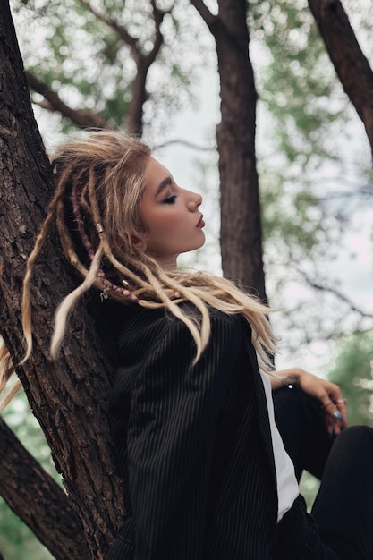 Une femme avec des dreadlocks est assise dans un arbre et regarde la caméra.