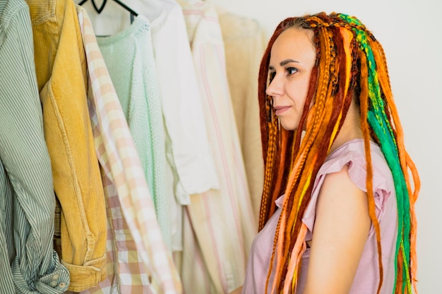 Femme avec des dreadlocks lumineux choisissant des vêtements dans le dressing Dressing moderne pour femmes légères avec diverses choses