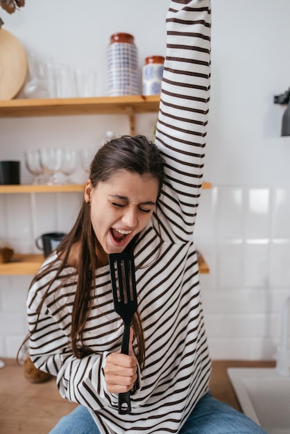 Femme drôle chantant dans une spatule tenant une spatule comme microphone