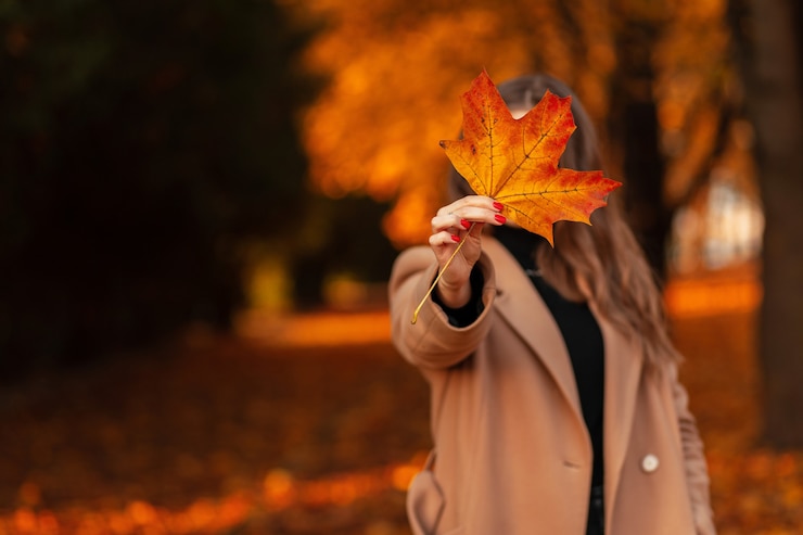 Photo une femme drôle dans un manteau à la mode beige montre une feuille d'automne de couleur jaune et se promène dans le parc doré à l'extérieur. feuillage d'automne se bouchent.
