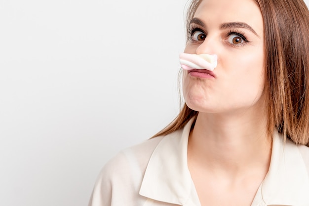 Une femme drôle fait de la moustache avec des bonbons à la guimauve sur fond blanc. Concept d'épilation et d'épilation.