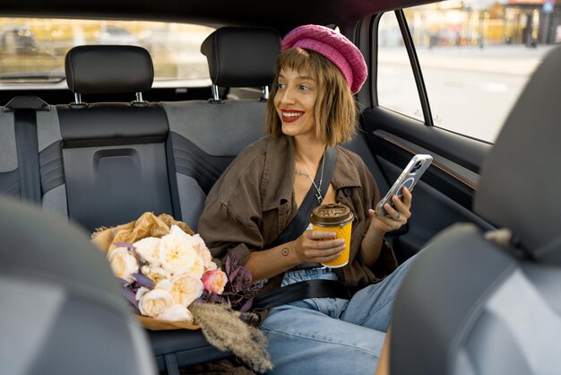 Femme avec du café et un téléphone sur le siège arrière d'une voiture