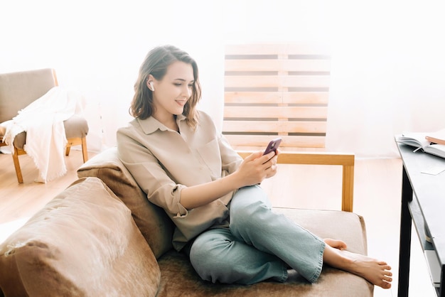 Photo une femme du millénaire heureuse avec des écouteurs sans fil regarde le téléphone lit des messages aime discuter commun