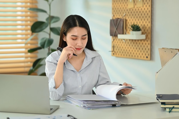 Femme économiste concentrée analysant les rapports sur les marchés financiers et utilisant un ordinateur portable à son poste de travail