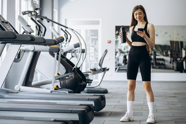 Femme écoutant de la musique et buvant de l'eau au gymnase