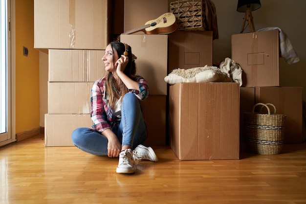 Une femme écoutant de la musique avec des écouteurs parmi des boîtes de carton concept d'une nouvelle maison