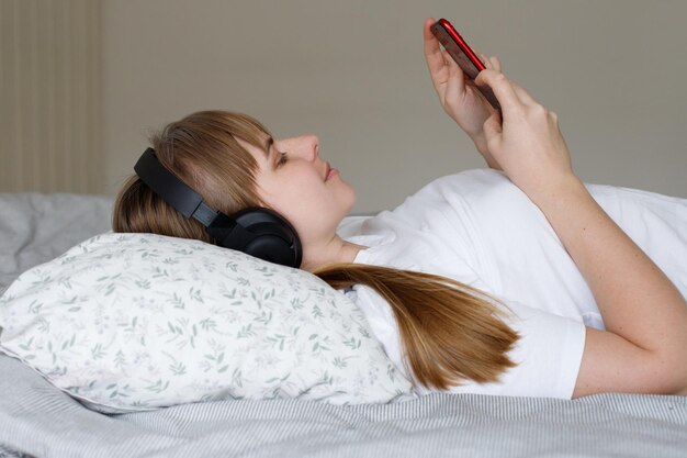 Photo femme avec des écouteurs écoutant de la musique avec un smartphone au lit à la maison