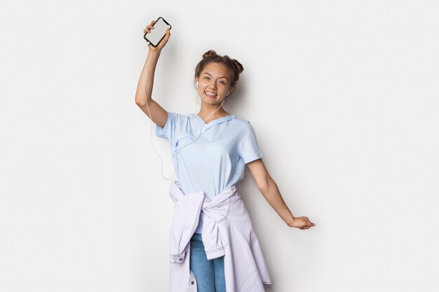 femme avec écouteurs montre à la caméra son écran de téléphone