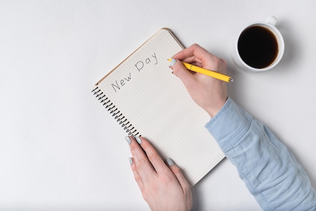 Femme écrit dans le carnet l'inscription NEW DAY Texte manuscrit Vue de dessus du bloc-notes et tasse de café