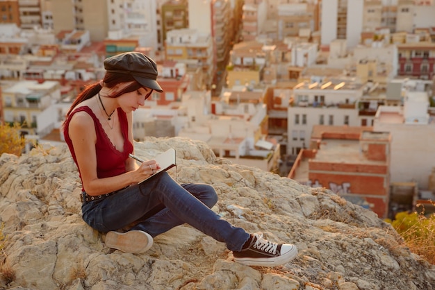 Une femme écrit dans son carnet des phrases et des pensées à l'extérieur au coucher du soleil