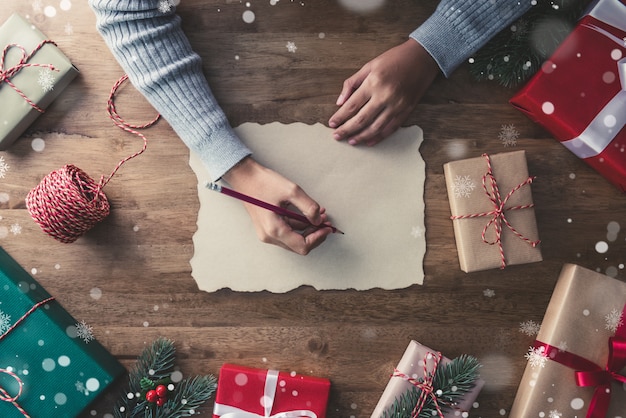 Une femme écrit sur du papier kraft au centre des cadeaux de Noël sur une table en bois