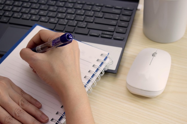 Une femme écrit ou prend des notes pendant une conférence ou étudie en ligne avec une souris d'ordinateur portable et une tasse de café