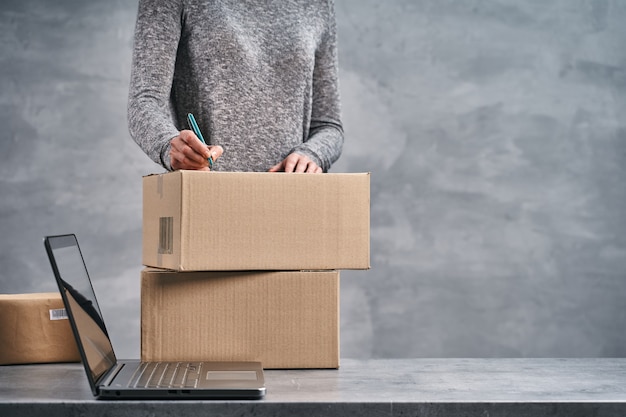 Femme écrivant des adresses sur les boîtes préparant des colis pour l'envoi de travail à domicile