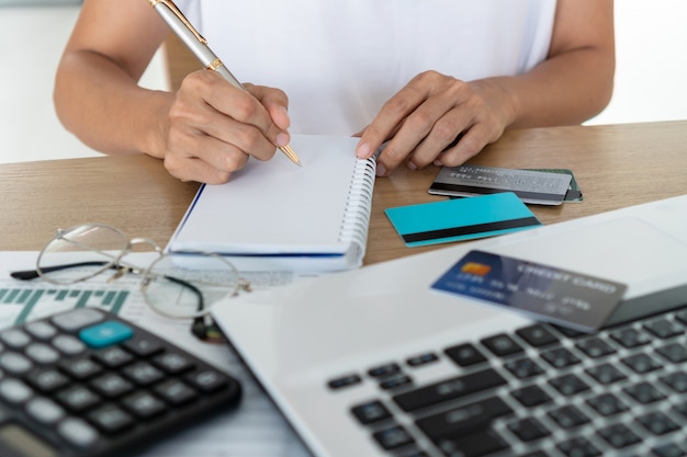 Femme écrivant sur ordinateur portable avec ordinateur, calculatrice et carte de crédit sur le bureau, le compte et le concept d'épargne.