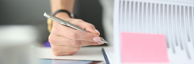 Femme écrivant avec un stylo à bille dans des documents avec des graphiques et des diagrammes à table in office