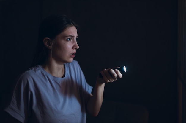 Femme effrayée tenant une lampe de poche dans l'obscurité et craignant la violence vol criminel
