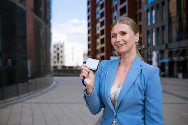 Femme élégante d'affaires dans une veste bleue tient un badge dans sa main d'un immeuble de bureaux