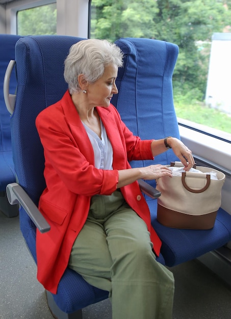 une femme élégante aux cheveux gris dans une veste rouge monte dans un train