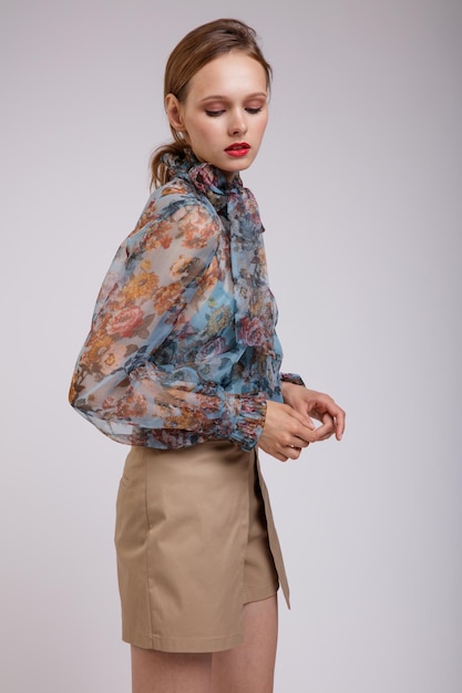 Femme élégante en blouse bleue avec noeud à motif floral sur le cou short beige sur fond blanc