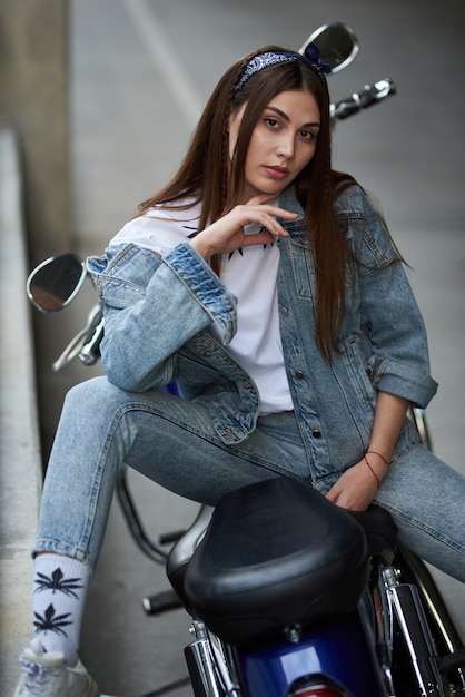 femme élégante dans un jean assis sur une moto garée près d'un centre commercial.