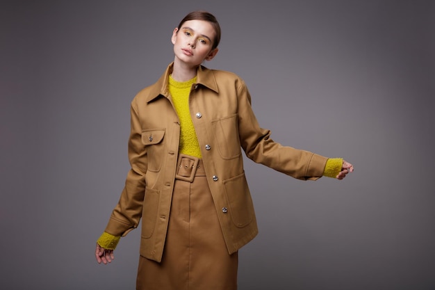 Femme élégante dans une jolie veste de sable beige marron jupe pull moutarde jaune sur fond gris