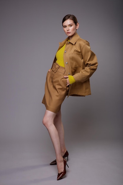 Femme élégante dans une jolie veste de sable beige marron jupe pull moutarde jaune sur fond gris