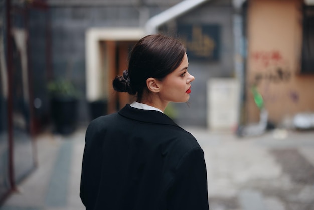 Femme élégante dans une veste noire marche le long de la rue de la ville avec son dos à la caméra suivez-moi