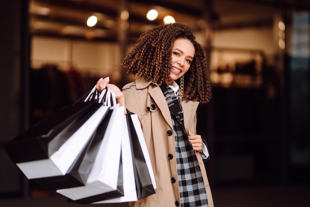 Femme élégante dans des vêtements à la mode avec des sacs à provisions près du centre commercial