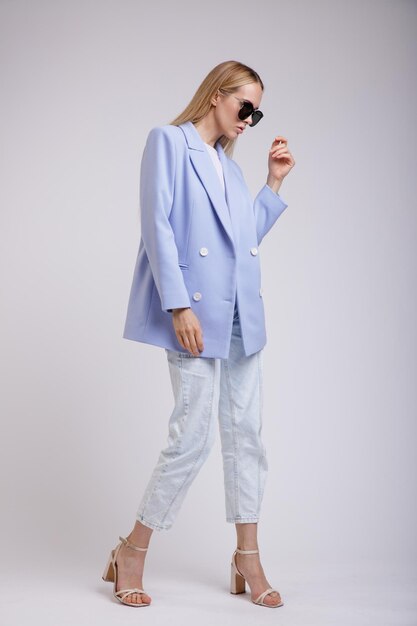 femme élégante en joli jean bleu, veste, lunettes de soleil sur fond blanc