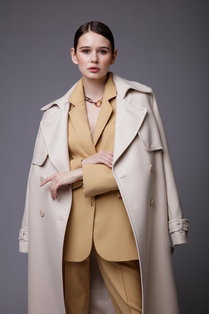 Femme élégante en joli manteau blanc sable beige costume veste pantalon pantalon accessoires fond gris