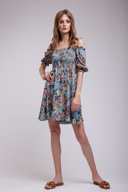 Femme élégante en jolie robe bleue avec motif floral posant sur fond blanc Silhouette mince