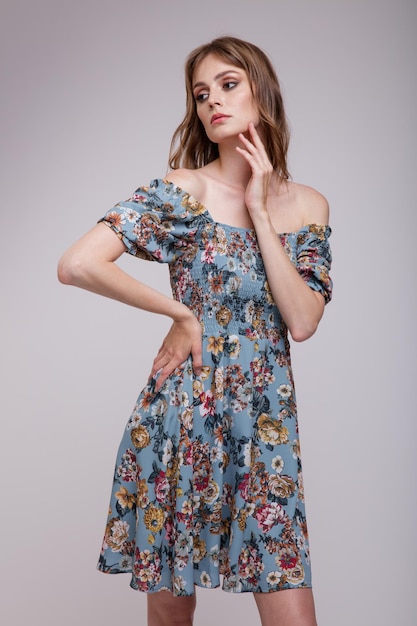 Femme élégante en jolie robe bleue avec motif floral posant sur fond blanc Silhouette mince