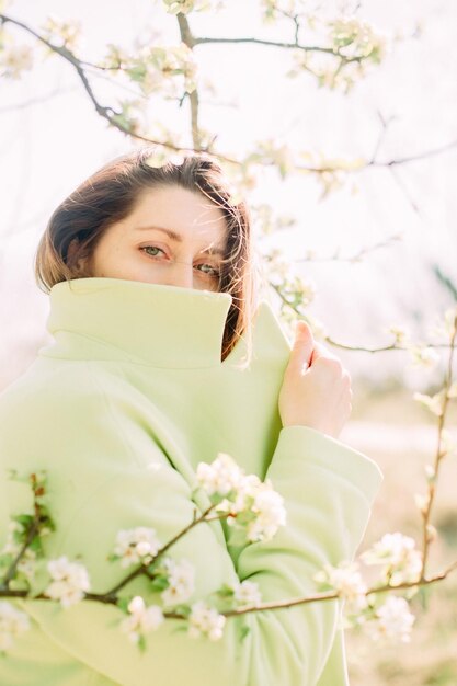 Femme élégante manteau vert fond floraison printanière