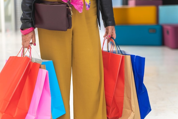 Une femme élégante et méconnaissable faisant ses courses avec des sacs colorés dans le centre commercial avant Noël.