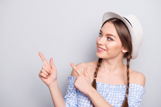 Femme élégante avec des nattes et un chapeau posant contre le mur blanc