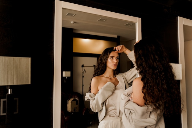 Femme élégante posant près du miroir et regardant son reflet