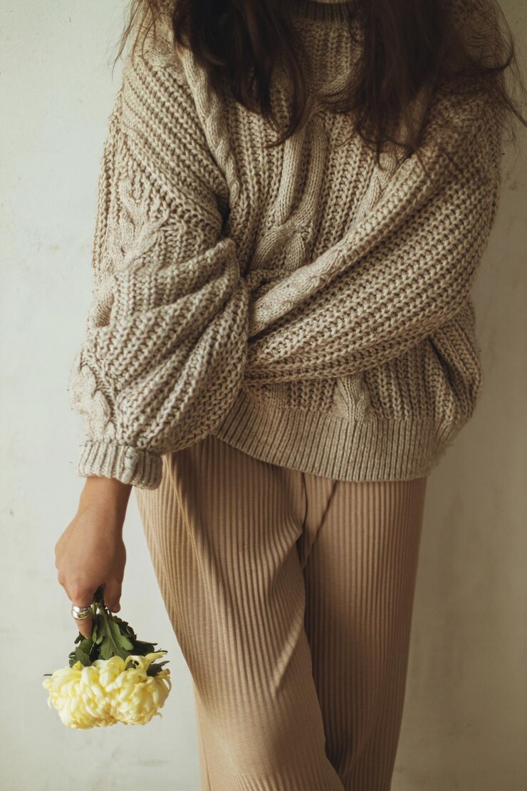 Femme élégante en pull à tricot confortable posant avec un chrysanthème à la main en gros plan sur le fond d'un mur rustique Moodie automne maison confortable Femme à la mode avec une esthétique d'automne de fleurs