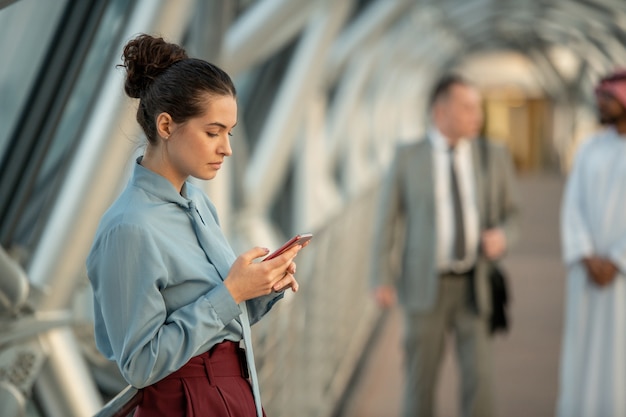 Femme élégante regardant le téléphone en se tenant devant la caméra