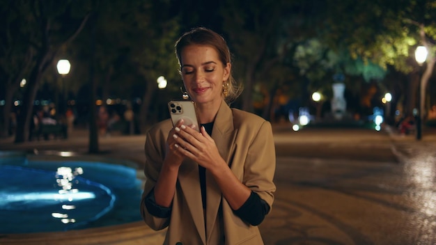 Une femme élégante répondant à un appel par smartphone dans la rue la nuit, une fille souriante parlant.