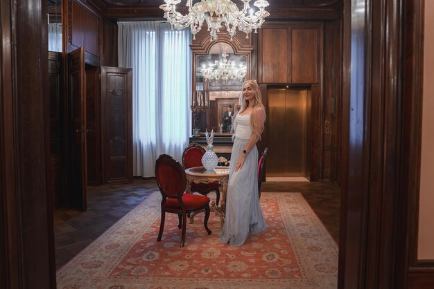 Femme élégante en robe bleue debout dans une chambre de luxe avec des lustres de la collection de Venise