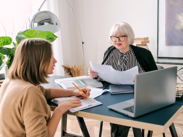 femme élégante senior avec une jeune femme discutant des tâches de travail au bureau