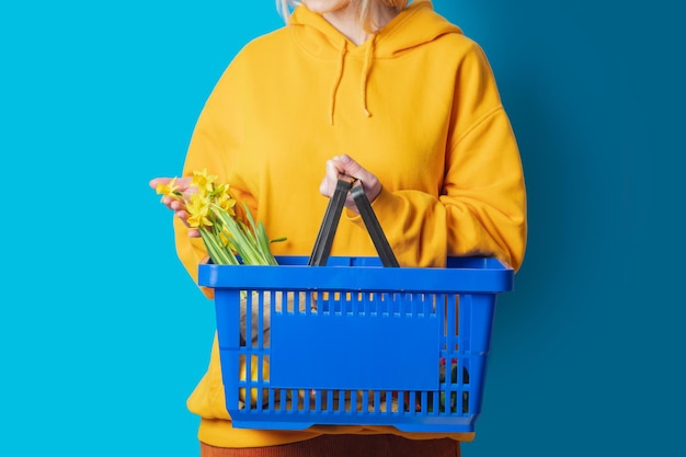 Femme élégante en sweat à capuche jaune avec panier bleu et fleurs sur fond bleu