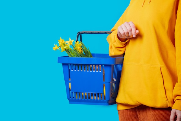 Photo femme élégante en sweat à capuche jaune avec panier bleu et fleurs sur fond bleu