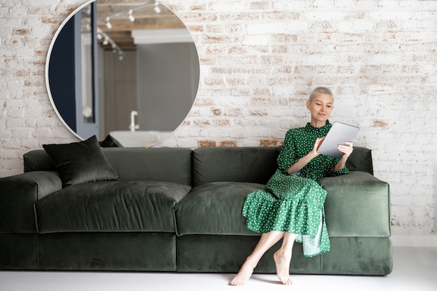 Femme élégante avec tablette numérique sur le canapé à la maison