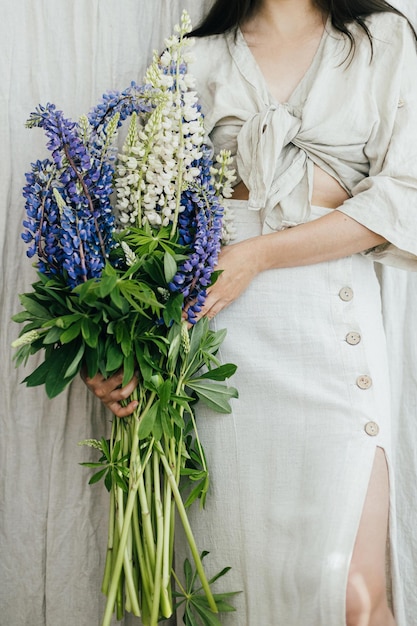 Femme élégante tenant un bouquet de lupin dans une chambre rustique en gros plan Collecte de fleurs sauvages d'été