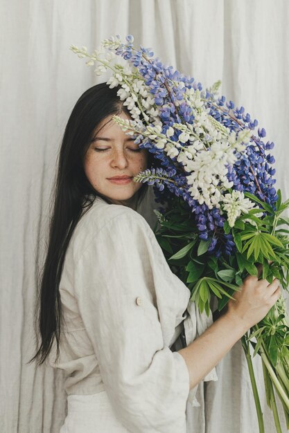 Femme élégante tenant un bouquet de lupin dans une chambre rustique Rassembler et organiser des fleurs sauvages d'été