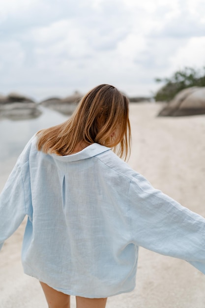 Femme élégante en tenue décontractée bleue posant sur une plage solitaire en nuageux xAweather Vue de dos