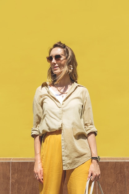 Femme élégante en tenue jaune contre un mur de couleur vive