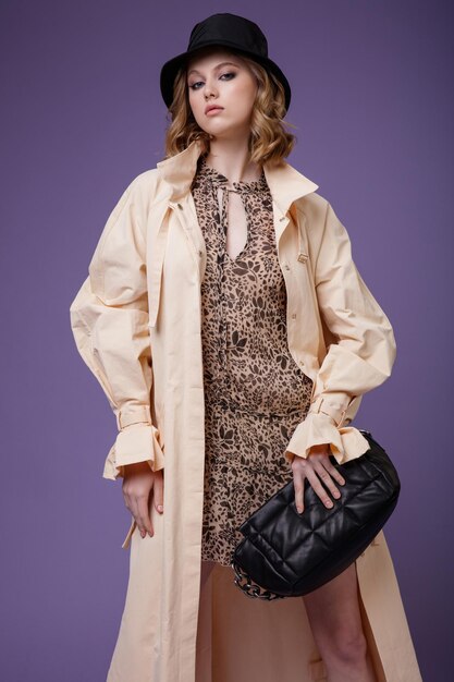 Femme élégante en trench-coat crème beige robe marron avec un sac à main bottes chapeau noir motif floral