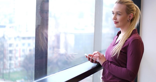 Femme élégante utilisant un téléphone portable par fenêtre dans un immeuble de bureaux